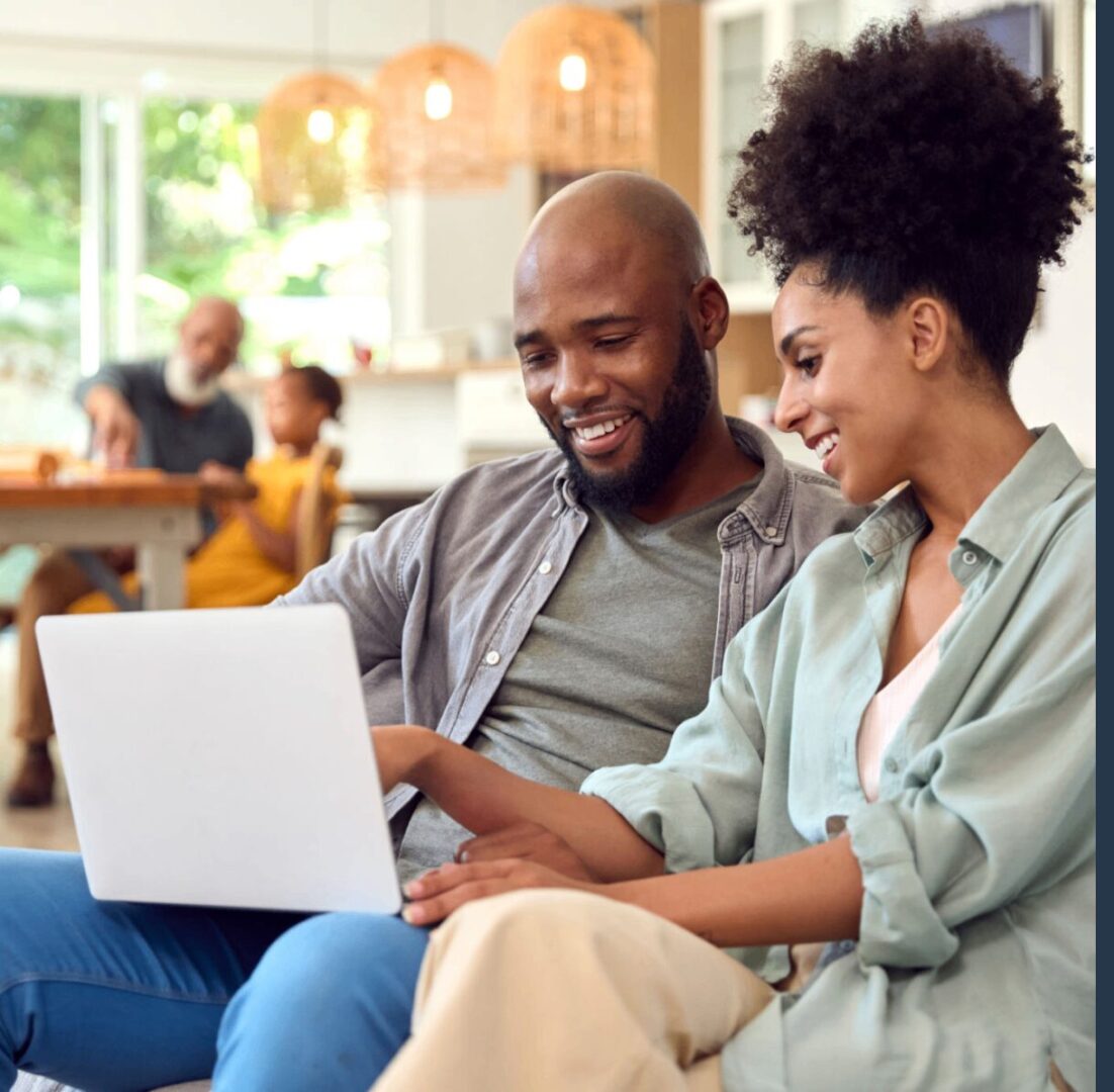 Couple smiling while using a laptop together.