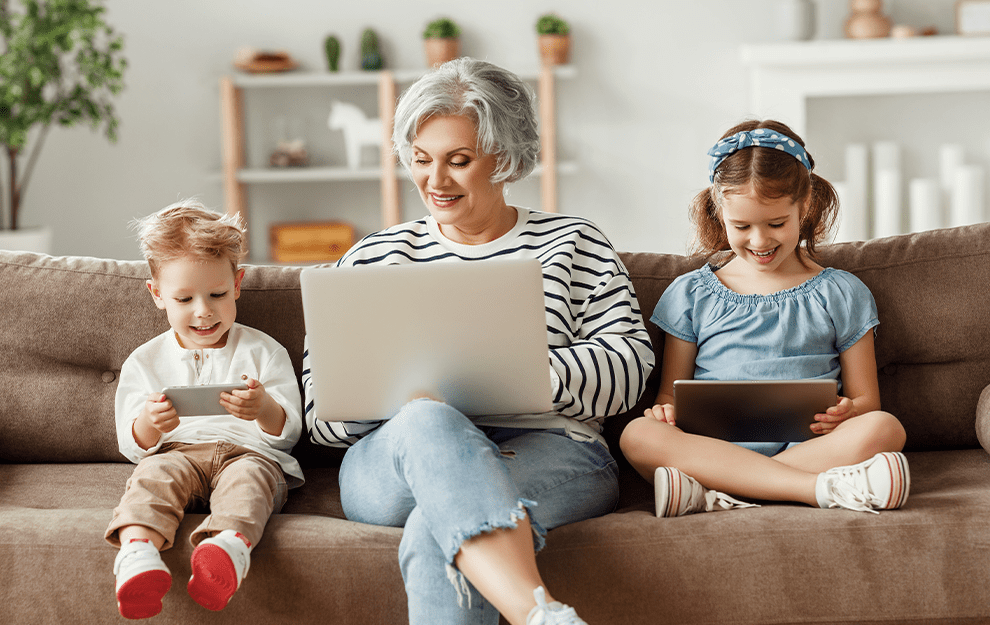Grandmother enjoying time with grandchildren using digital devices at home.