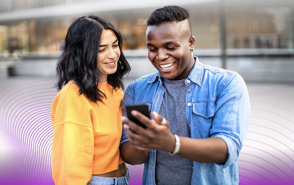 Two friends happily looking at a phone together outdoors.