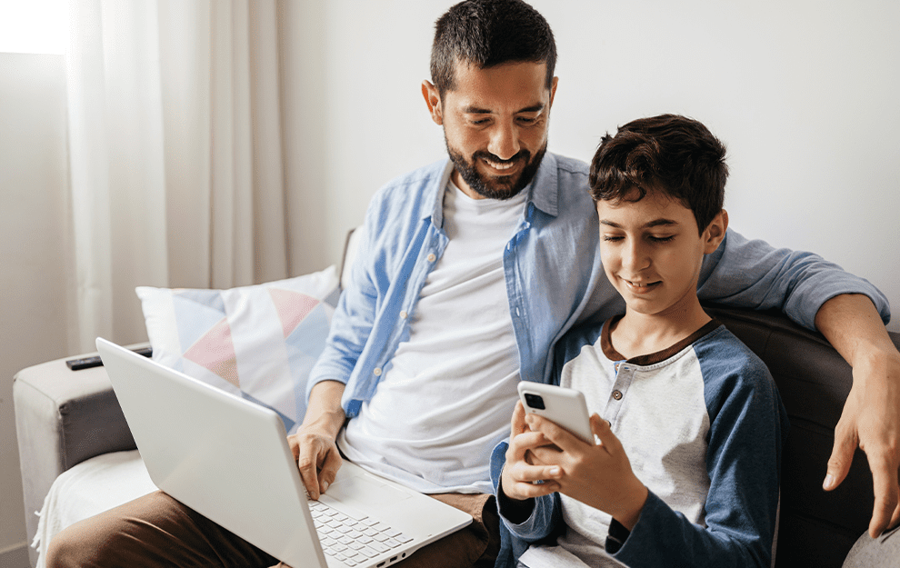 A father and son bonding with laptop and smartphone at home.
